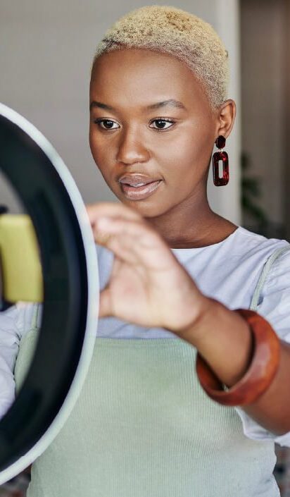 A Black woman sets up her phone in front of a round light, indicating she might be YouTuber and knows just how much do YouTubers make.