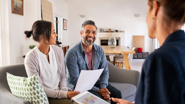 Three people gather around a sofa to discuss the pros and cons of a living trust.