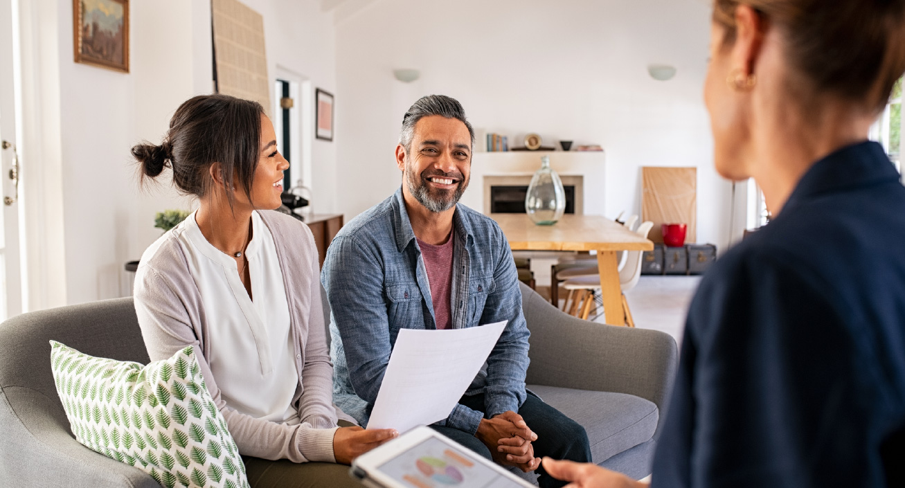 Three people gather around a sofa to discuss the pros and cons of a living trust.