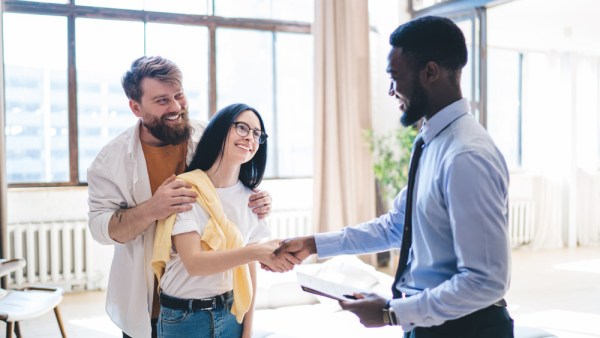 Image of black man holding clipboard and shaking hands with a white woman while her husband stands behind her.