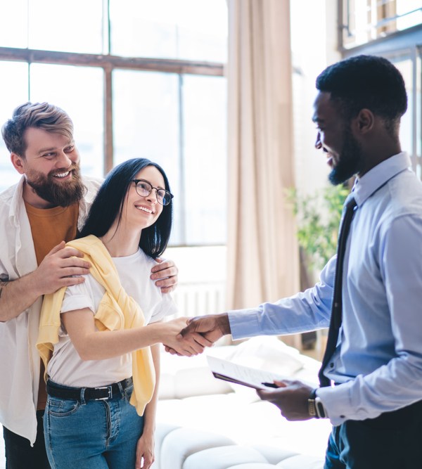 Image of black man holding clipboard and shaking hands with a white woman while her husband stands behind her.