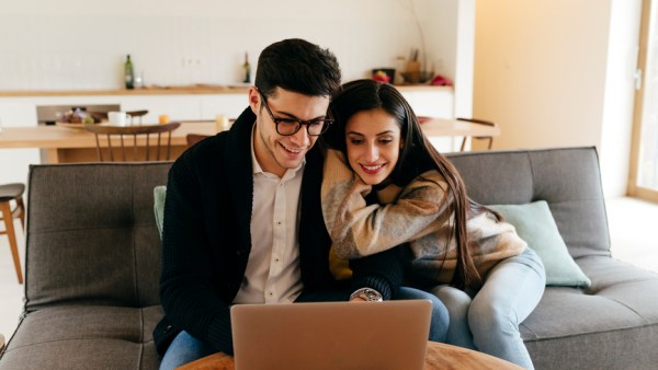 Man Using Laptop with Partner On Sofa