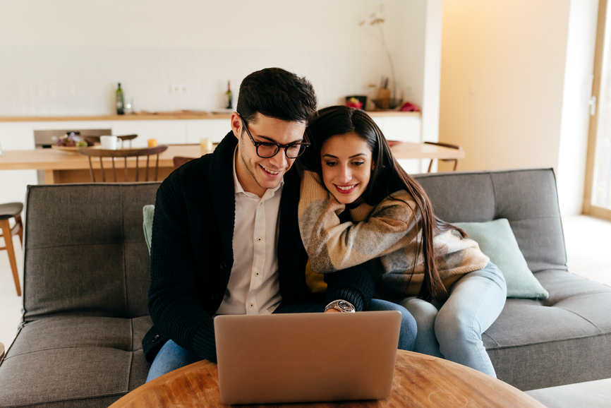 Man Using Laptop with Partner On Sofa