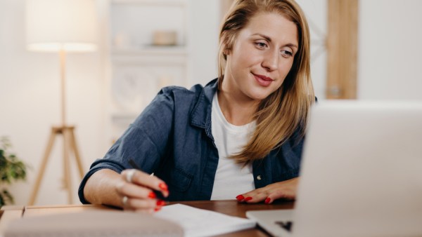 Woman taking notes and looking at laptop