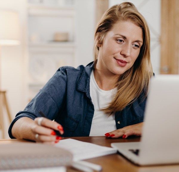 Woman taking notes and looking at laptop