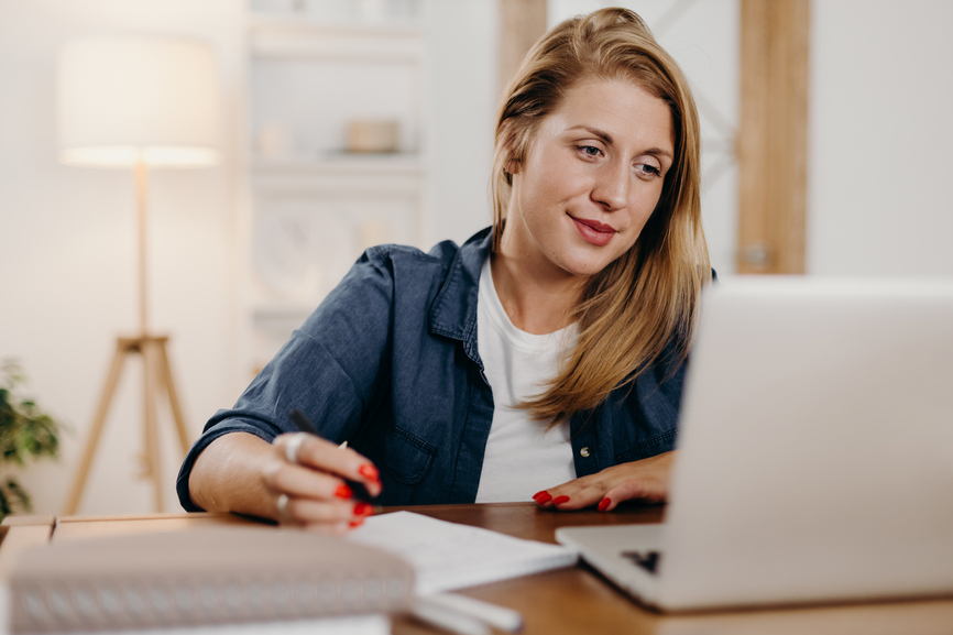 Woman taking notes and looking at laptop