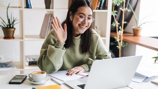 woman-smiling-and-waving-to-video-call-on-laptop