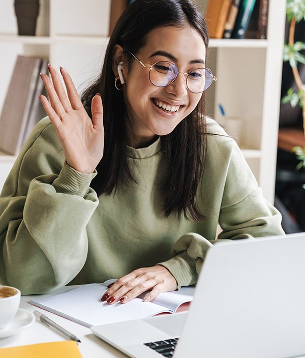 woman-smiling-and-waving-to-video-call-on-laptop