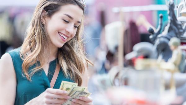 A woman is counting the cash she has in her hand while smiling at objects for sale, indicating she’s using her fiat money to buy something.