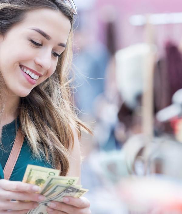 A woman is counting the cash she has in her hand while smiling at objects for sale, indicating she’s using her fiat money to buy something.