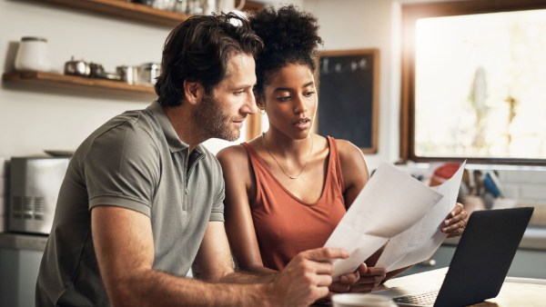 A couple sits at their kitchen table in front of their computer while looking at their bank statements, indicating they want to start having better money habits.