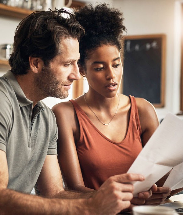 A couple sits at their kitchen table in front of their computer while looking at their bank statements, indicating they want to start having better money habits.