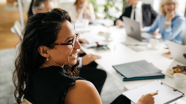 A woman sits at a work meeting and smiles at her cowokers, indicating she believes she has one of the most fulfilling jobs.