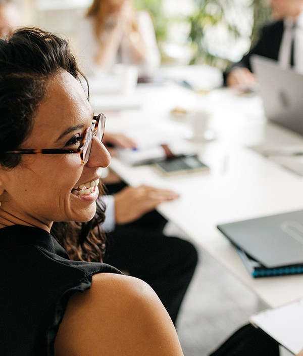 A woman sits at a work meeting and smiles at her cowokers, indicating she believes she has one of the most fulfilling jobs.