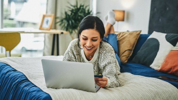 A woman lays on her bed while using her computer and holding her credit card, indicating she just learned about how credit cards work.