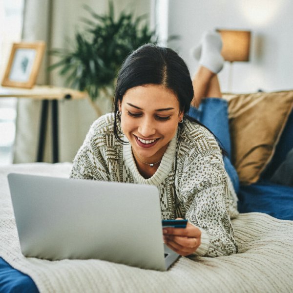 A woman lays on her bed while using her computer and holding her credit card, indicating she just learned about how credit cards work.