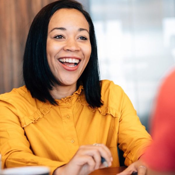 A women during a meeting smiles while speaking to another women, indicating she's learned how to ask for a raise.