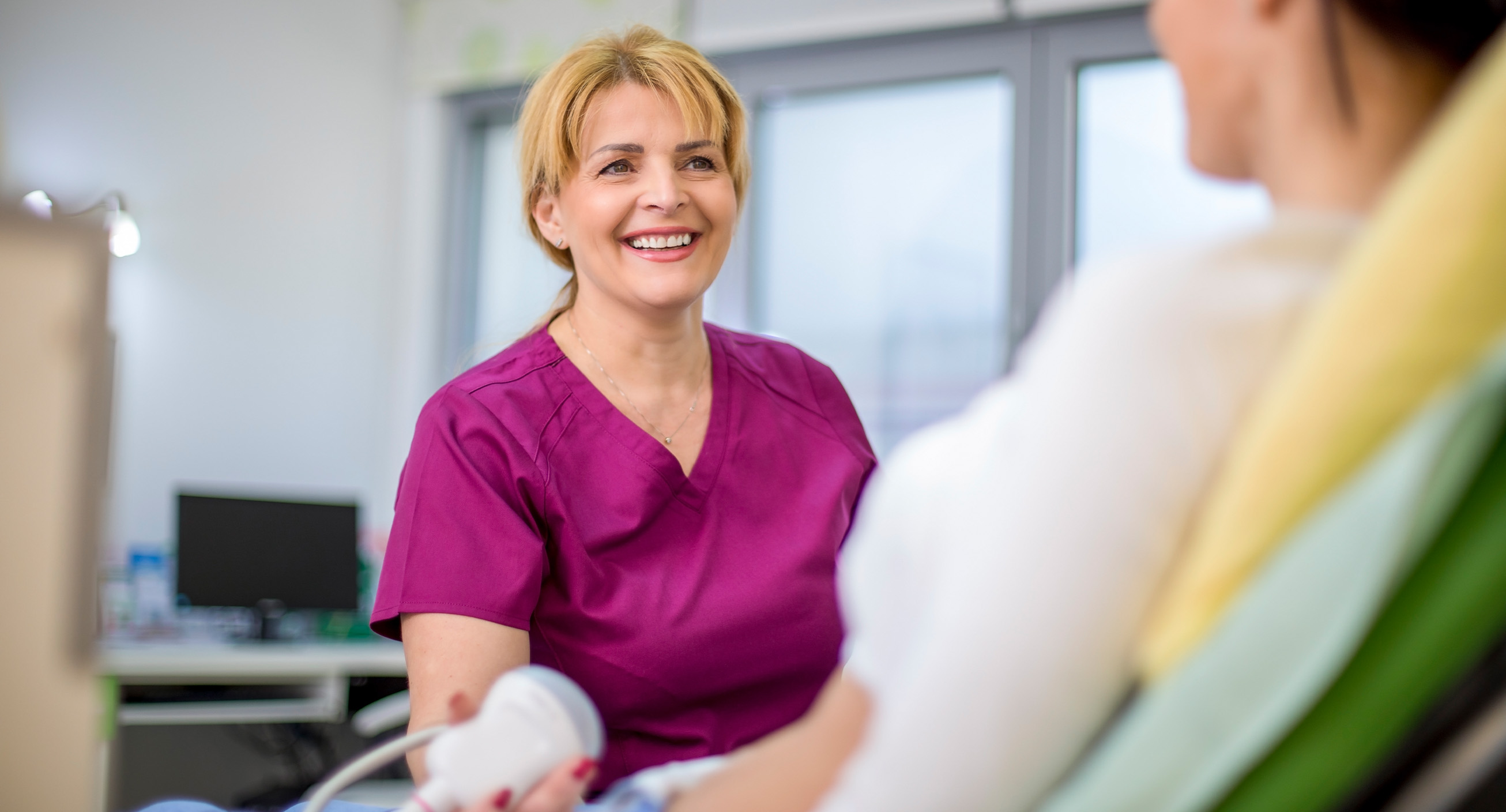 An ultrasound technician, one of the highest paying trade jobs, smiles at her patient while operating imaging equipment for ultrasounds.