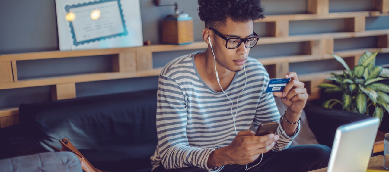 man in a striped shirt gazes at his tablet with a credit card in hand, indicating he might be reading about investing for beginners.