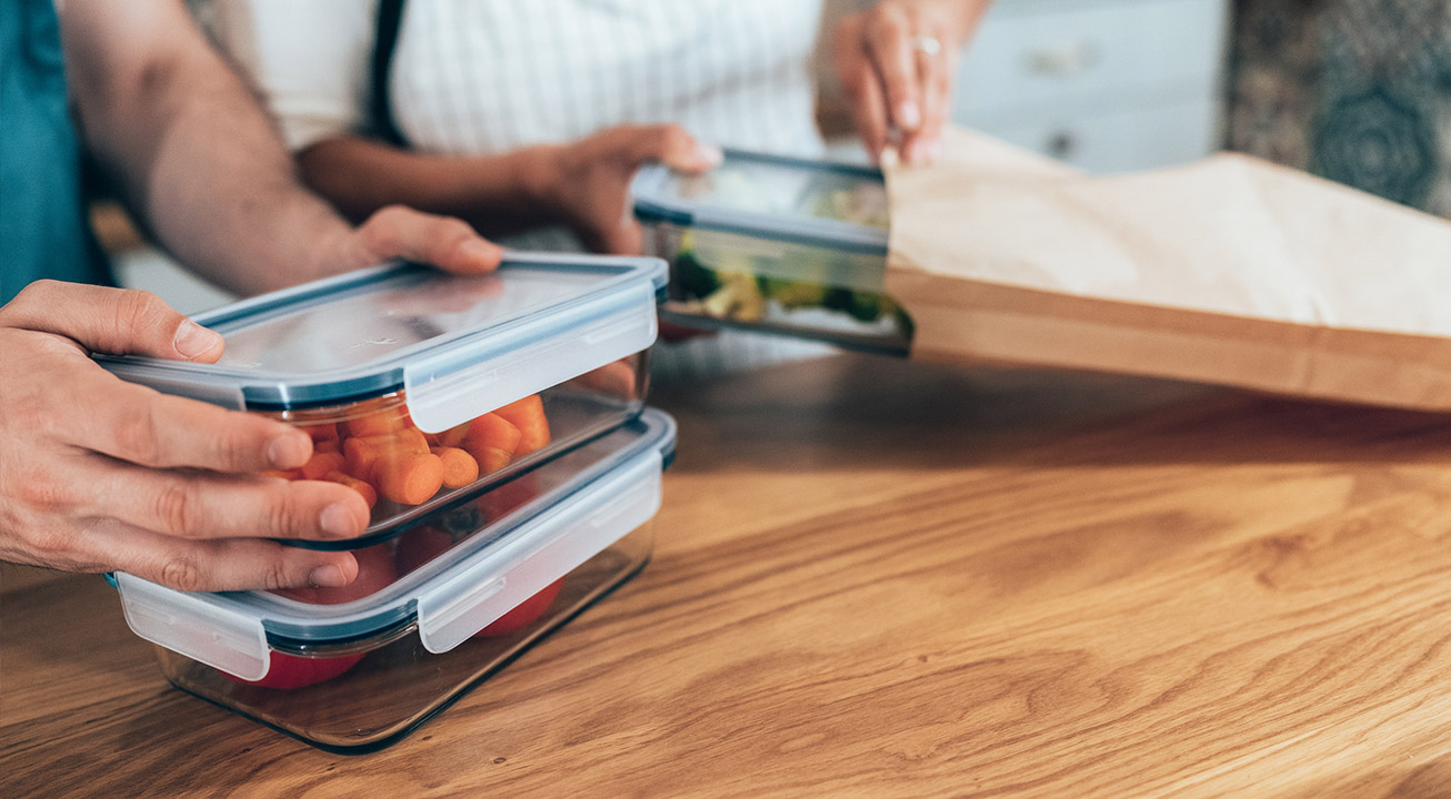 Someone packing lunch in glass containers while another person puts containers into a paper bag.